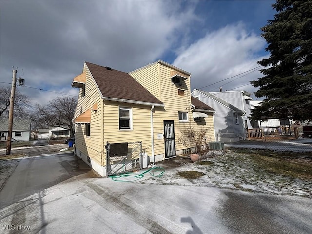 rear view of property featuring central air condition unit and roof with shingles