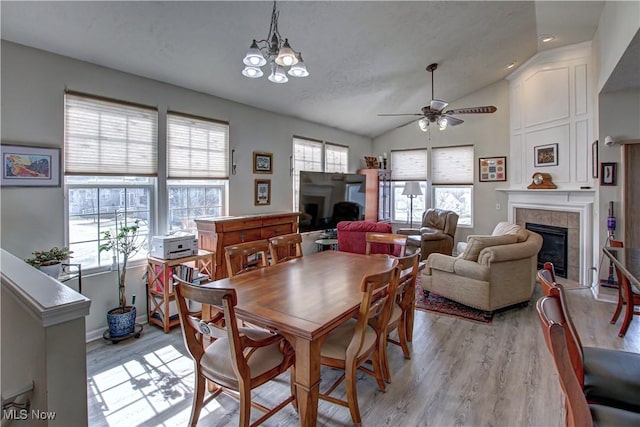 dining room with light wood-type flooring, a fireplace, lofted ceiling, and ceiling fan with notable chandelier