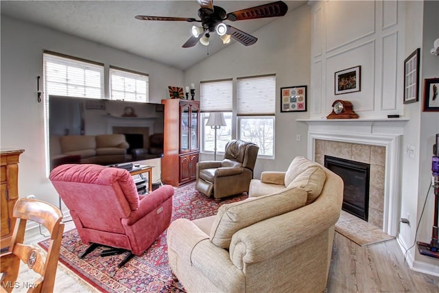 living area featuring lofted ceiling, light wood finished floors, a ceiling fan, and a tile fireplace