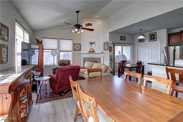 dining space with light wood-style flooring, a tile fireplace, lofted ceiling, and a ceiling fan