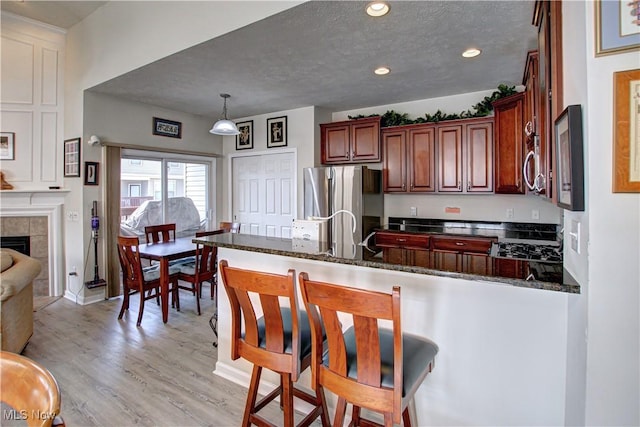 kitchen with a breakfast bar area, light wood-style floors, freestanding refrigerator, a textured ceiling, and a peninsula