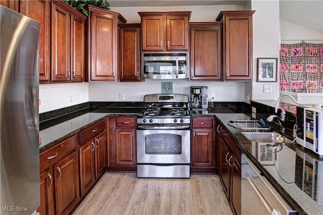 kitchen with dark stone counters, appliances with stainless steel finishes, a sink, and light wood-style flooring