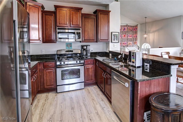 kitchen with dark stone counters, lofted ceiling, light wood-style flooring, appliances with stainless steel finishes, and a peninsula