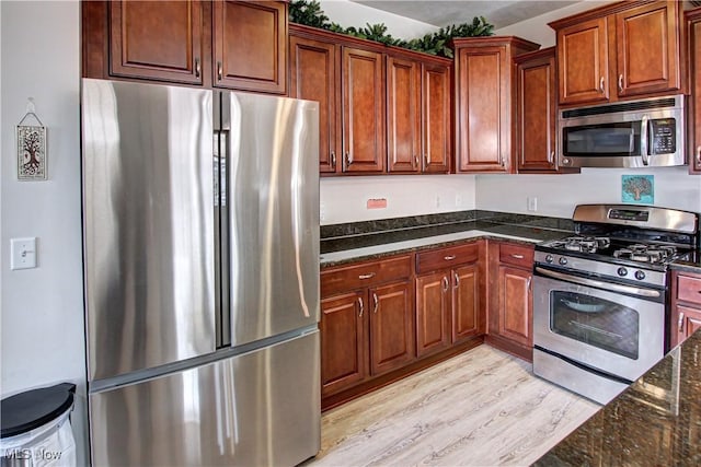 kitchen with dark stone counters, appliances with stainless steel finishes, brown cabinetry, and light wood-style floors