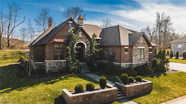 english style home with a front yard, stone siding, a garden, and brick siding