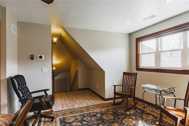 sitting room featuring baseboards, visible vents, a textured ceiling, and an upstairs landing