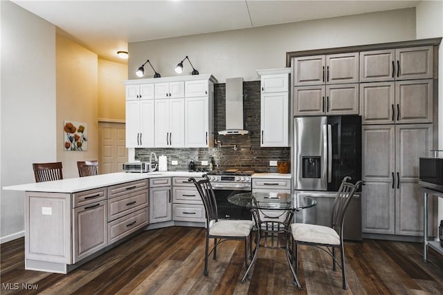 kitchen with dark wood-style flooring, stainless steel appliances, light countertops, wall chimney range hood, and backsplash