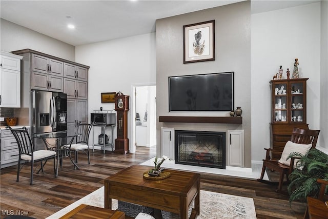 living room with dark wood-style flooring, a glass covered fireplace, and recessed lighting