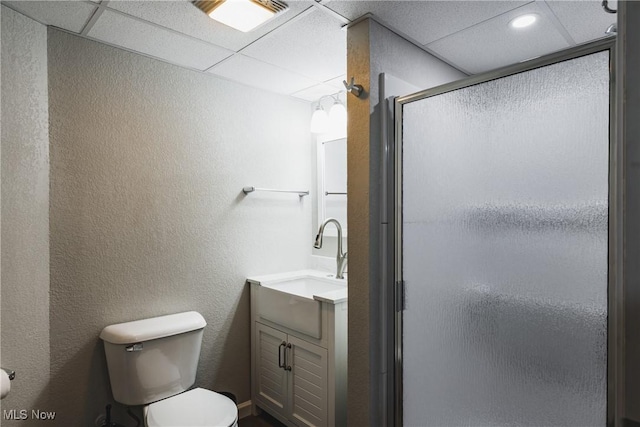 full bathroom with toilet, a stall shower, a drop ceiling, and vanity