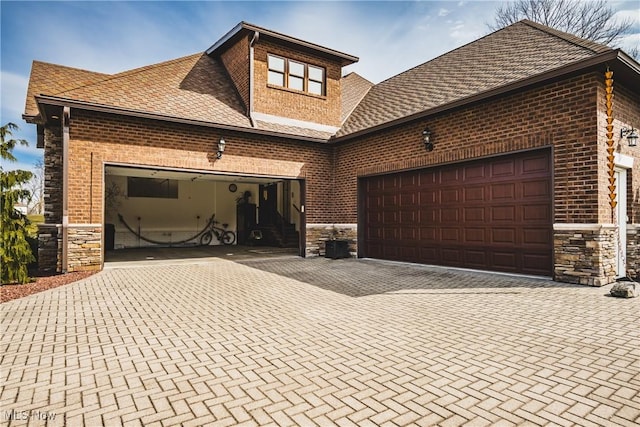 view of front of home featuring an attached garage, stone siding, and decorative driveway