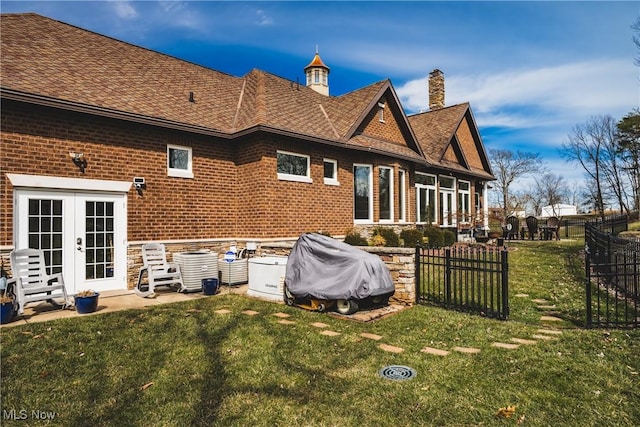 rear view of house featuring french doors, brick siding, a yard, a chimney, and fence