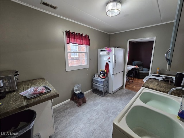 kitchen with baseboards, visible vents, freestanding refrigerator, crown molding, and a sink