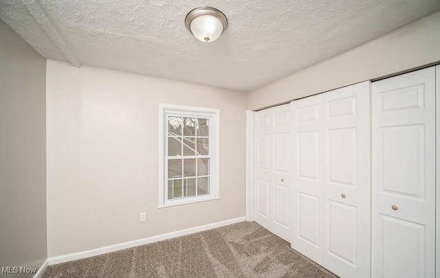 unfurnished bedroom with a textured ceiling, a closet, carpet, and baseboards