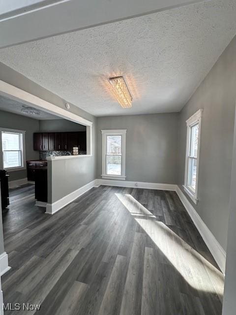 unfurnished living room with a textured ceiling, dark wood-style flooring, and baseboards