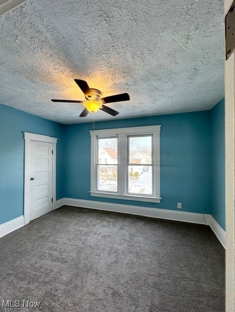 unfurnished room with a textured ceiling, baseboards, dark colored carpet, and a ceiling fan