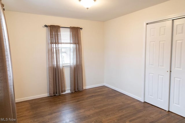 unfurnished bedroom with dark wood-type flooring, a closet, and baseboards