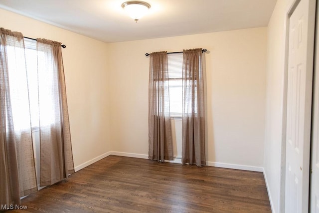 empty room with dark wood-style floors, a healthy amount of sunlight, and baseboards