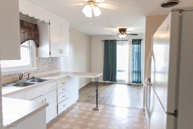 kitchen featuring visible vents, white cabinets, freestanding refrigerator, light floors, and a sink