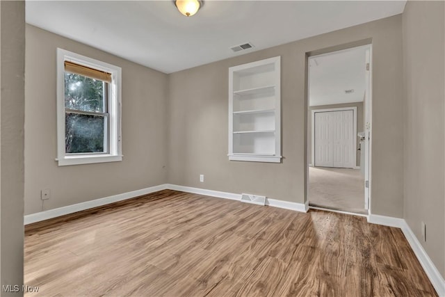 empty room featuring built in shelves, wood finished floors, visible vents, and baseboards