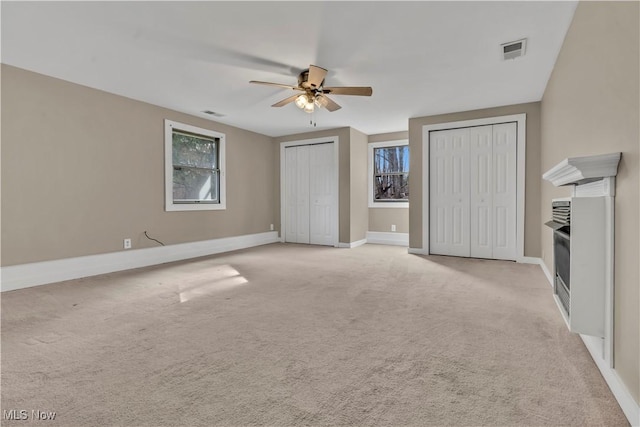 unfurnished bedroom with multiple closets, visible vents, light carpet, and baseboards