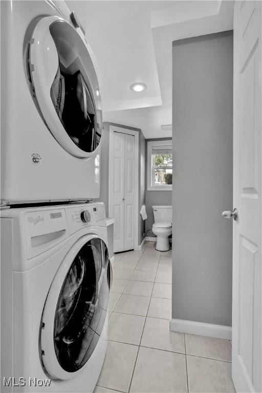 laundry room with light tile patterned floors, laundry area, baseboards, and stacked washer / drying machine