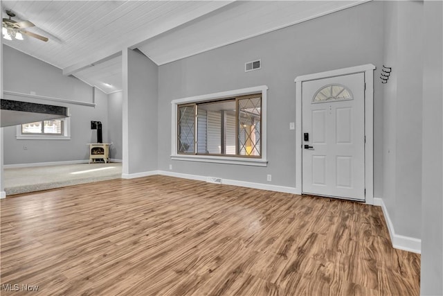 entrance foyer with wood finished floors, visible vents, baseboards, vaulted ceiling, and a wood stove