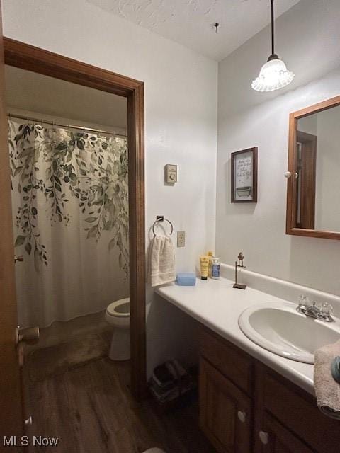 bathroom with toilet, a shower with curtain, wood finished floors, and vanity