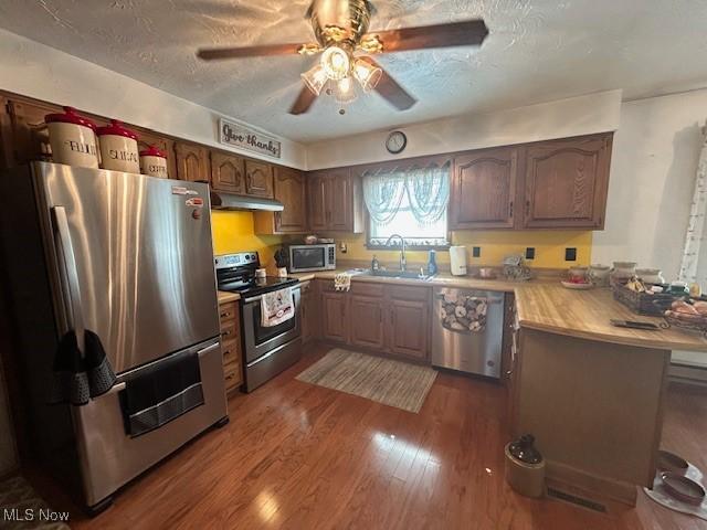 kitchen with wood finished floors, light countertops, stainless steel appliances, under cabinet range hood, and a sink