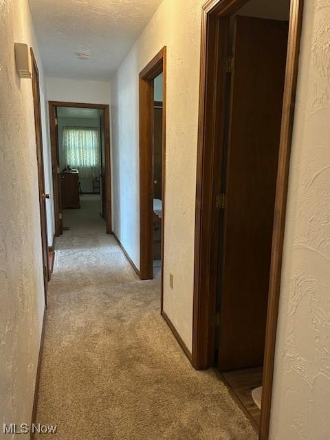 hall with light carpet, a textured ceiling, and a textured wall