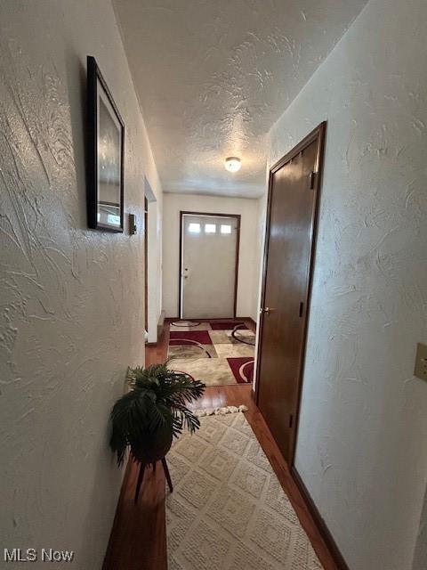 doorway to outside with a textured ceiling, a textured wall, and wood finished floors