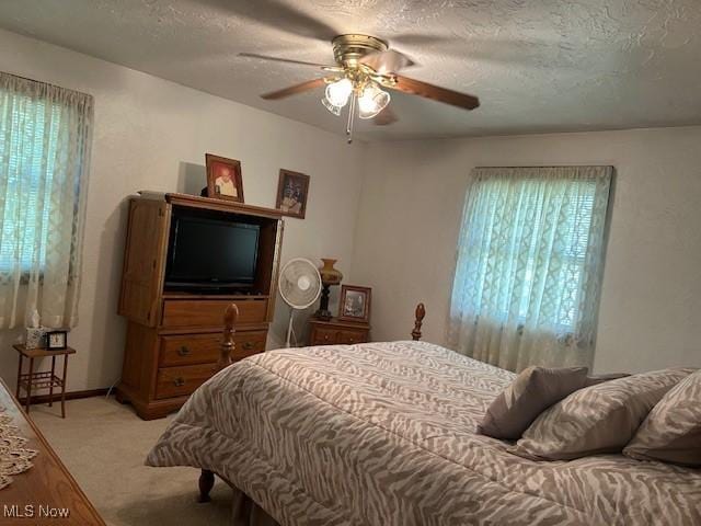 bedroom featuring light carpet, ceiling fan, baseboards, and a textured ceiling