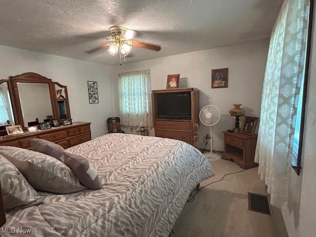 bedroom with a ceiling fan, light colored carpet, visible vents, and a textured ceiling