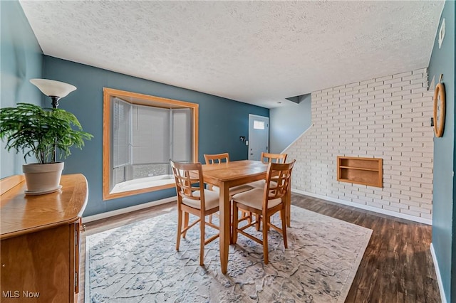 dining area with a textured ceiling, brick wall, wood finished floors, and baseboards