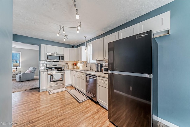 kitchen with stainless steel appliances, decorative backsplash, white cabinetry, a sink, and light wood-type flooring