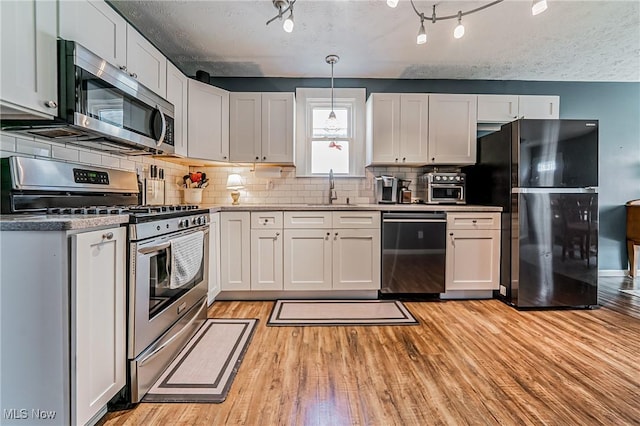 kitchen featuring decorative backsplash, appliances with stainless steel finishes, white cabinets, a sink, and light wood-type flooring