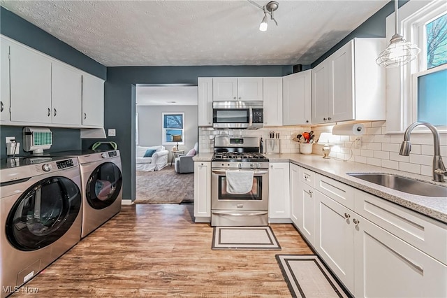 kitchen with stainless steel appliances, a sink, white cabinets, light wood finished floors, and washing machine and clothes dryer