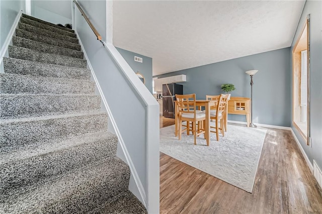 stairway featuring visible vents, a textured ceiling, baseboards, and wood finished floors