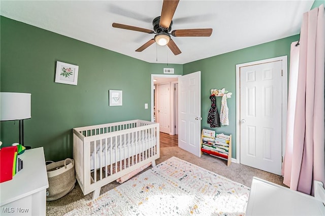 carpeted bedroom with a nursery area, ceiling fan, visible vents, and baseboards