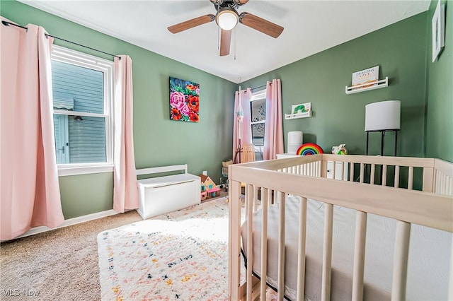 carpeted bedroom featuring multiple windows, a crib, and baseboards