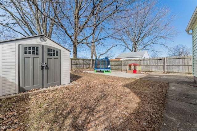 view of yard with a trampoline, a fenced backyard, an outdoor structure, and a shed