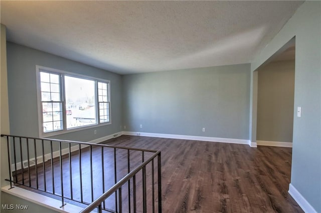 unfurnished room featuring a textured ceiling, dark wood-style flooring, and baseboards