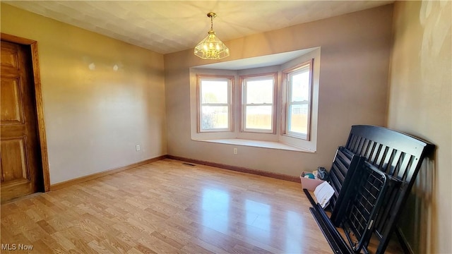 empty room featuring visible vents, light wood-style flooring, baseboards, and an inviting chandelier