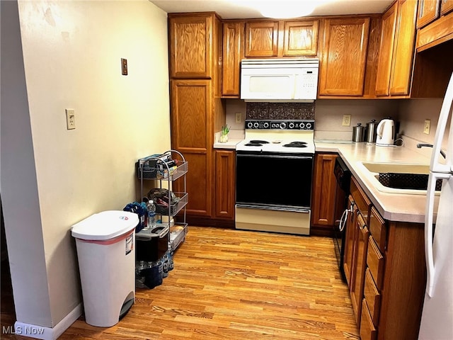 kitchen featuring white appliances, brown cabinetry, light countertops, light wood-style floors, and a sink