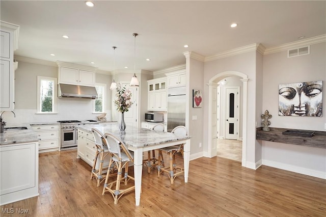 kitchen with arched walkways, decorative columns, a sink, high quality appliances, and under cabinet range hood