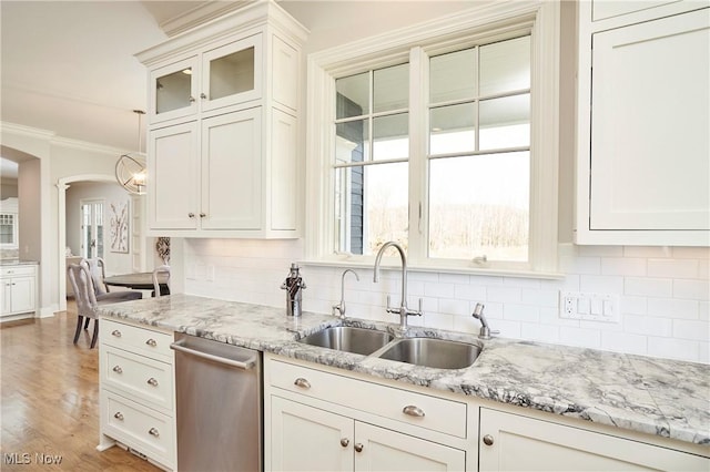 kitchen with light stone counters, crown molding, tasteful backsplash, stainless steel dishwasher, and a sink