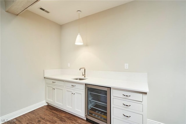 bar featuring dark wood finished floors, visible vents, a sink, beverage cooler, and baseboards