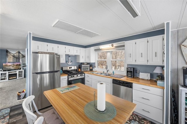 kitchen with butcher block counters, appliances with stainless steel finishes, white cabinets, and a sink