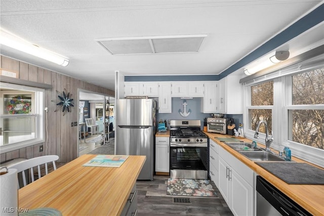 kitchen featuring stainless steel appliances, butcher block counters, wood walls, a sink, and white cabinetry