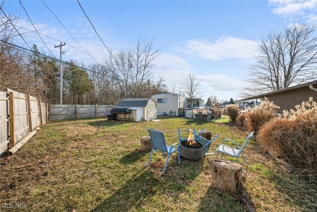 view of yard featuring a storage unit, a fenced backyard, a fire pit, and an outbuilding