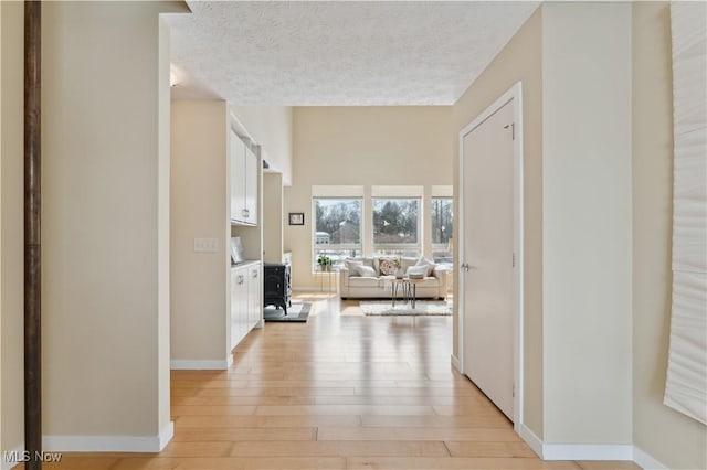 hallway with light wood-style floors, a textured ceiling, and baseboards